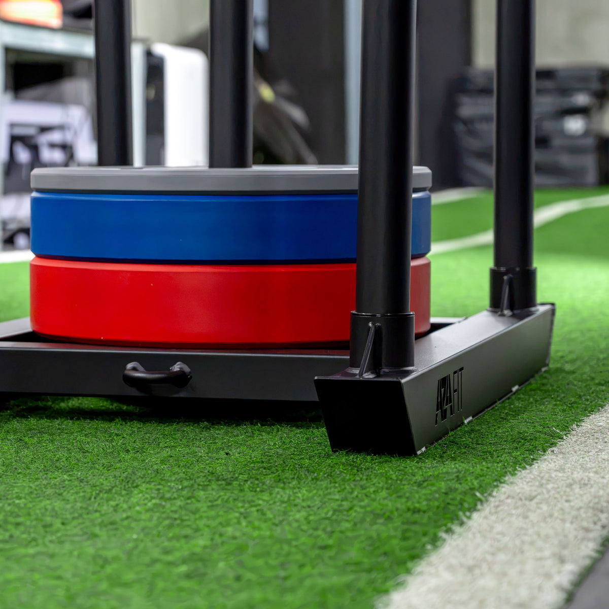 Pista de relva artificial GRASS com trenó carregado de discos, para exercícios de sled push em ginásio.