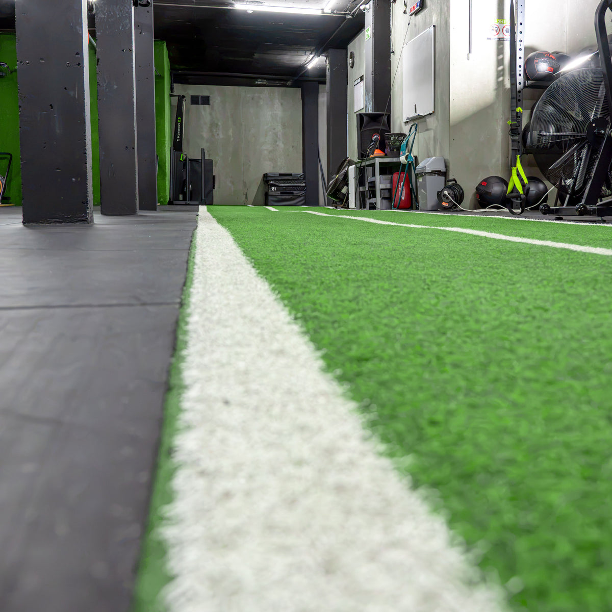 Pista de relva artificial GRASS instalada num ginásio, com linhas brancas a delimitar a área de treino funcional.